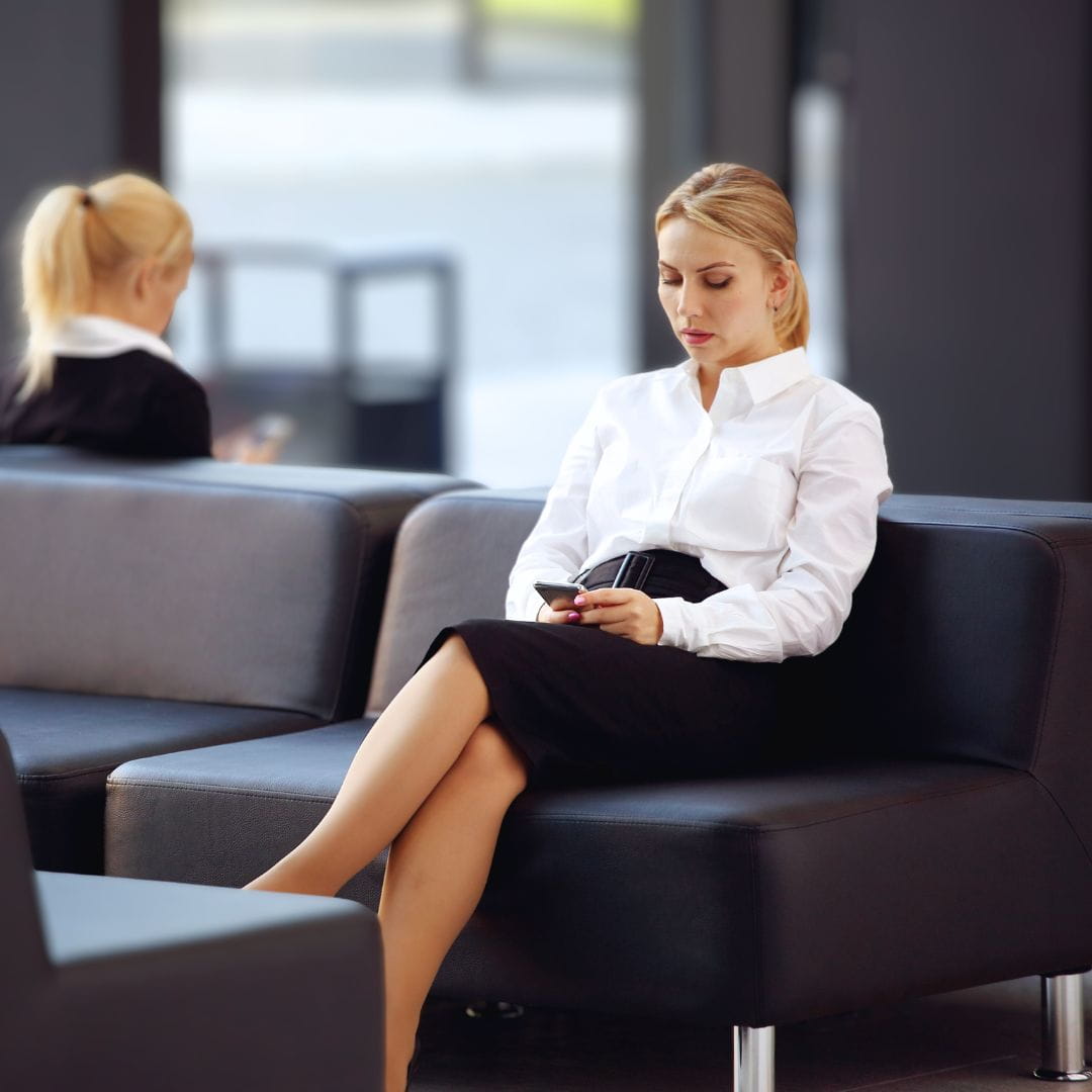 Businesswoman relaxing on a leather sofa in a VIP airport terminal while checking her phone before departure.